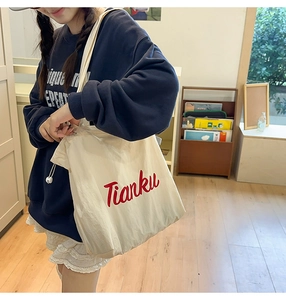 Detail of red Tianku embroidery on beige nylon tote bag with drawstring closure
