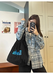 Detail shot of black nylon tote bag with drawstring closure and blue artistic Takmi logo