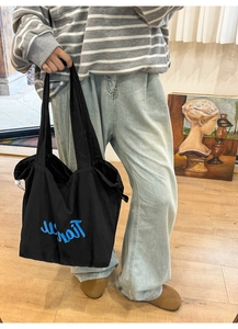 Detail of minimalist black nylon tote bag featuring blue cursive embroidery for women