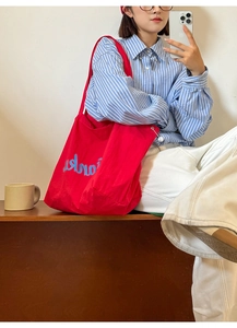 Detail shot of a large red canvas tote bag with drawstring and blue lettering print
