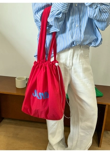 Detail of red nylon tote bag featuring blue MAR embroidery and white drawstring closure