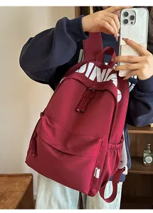 Detail of burgundy waterproof nylon backpack featuring white letter print and woven pullers