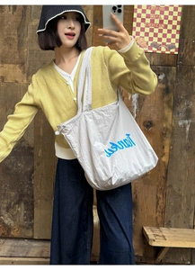 Detail shot of a large beige canvas tote bag with blue artistic lettering and drawstring