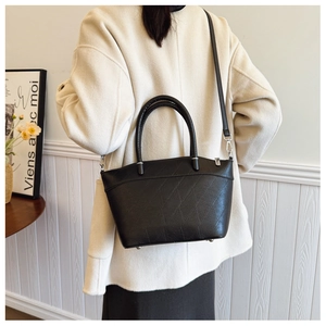 Detail view of the black bucket bag with geometric embossed pattern worn by a model
