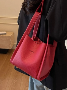 Red lychee grain leather bucket bag with handle held by model in black suit