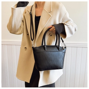 Detail of black quilted bucket bag featuring a textured pattern and detachable shoulder strap