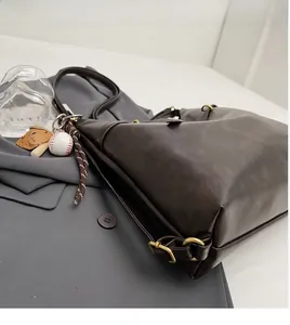 Detalle de bolso tote marrón oscuro con herrajes dorados y colgante de béisbol
