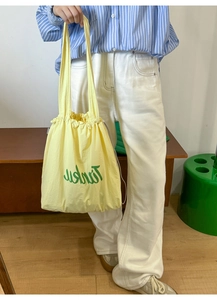 Detailed view of the yellow nylon tote bag with green typography and drawstring closure