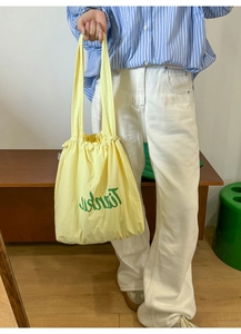 Detail shot of pale yellow nylon tote bag with drawstring closure and green lettering