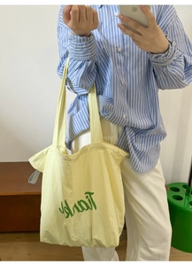 Detail of light yellow nylon tote bag with green Thanks print and wide shoulder straps