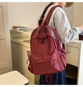 Close-up of a burgundy canvas backpack with letter print and front zipper pocket detail