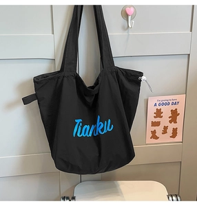 Close-up of black nylon drawstring tote bag with blue Tianku lettering on a textured wall