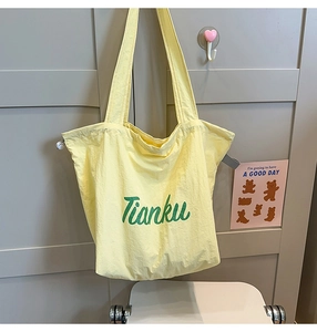 Detail view of lightweight pale yellow nylon tote bag featuring green Tianku branding