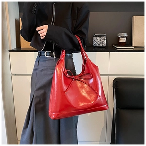 Close-up of red glossy oil-wax leather tote bag with a decorative bow detail