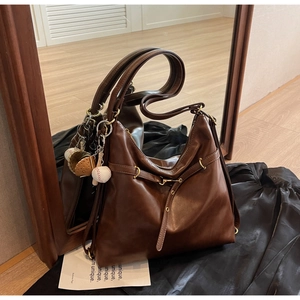 Detalle del bolso tote de cuero marrón oscuro con colgante de béisbol y herrajes dorados