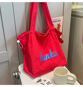 Detail of red nylon tote bag featuring blue letter print and white side drawstrings