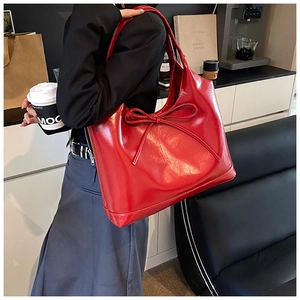 Detail of red glossy patent leather tote bag featuring a bow accent in a cafe setting