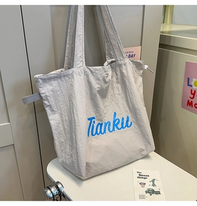 Detail of grey nylon tote bag with light blue Tianku lettering and drawstring side strap