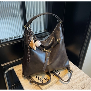 Detalle de bolso hobo de cuero brillante marrón oscuro con colgante de béisbol en mármol
