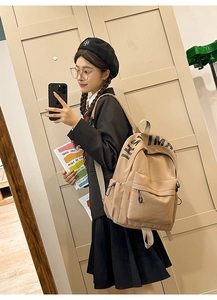Close-up of beige canvas backpack featuring bold black lettering and functional pockets