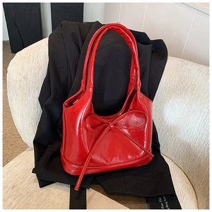 Close-up of vibrant red wax-leather tote with oversized bow detail on black suit