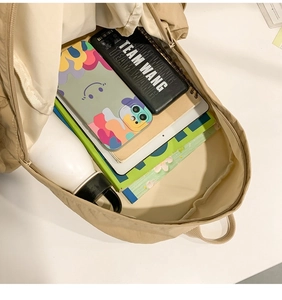 Top view of a beige minimalist backpack showing large interior storage with books and tablet