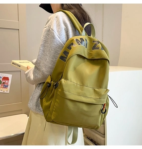 Detail view of the green nylon backpack featuring a front pocket and side pockets
