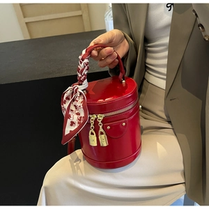 Détail du sac cylindrique rouge avec finitions dorées et foulard en soie au manche