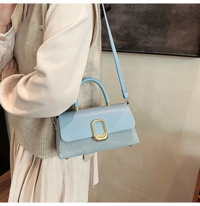 Detail of light blue crossbody bag featuring gold buckle and woven leather texture