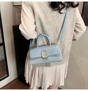 Detail of light blue crossbody bag featuring woven texture and golden square lock