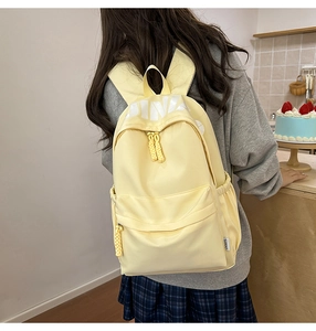 Detail view of the pale yellow canvas backpack with white letter printing and side woven label