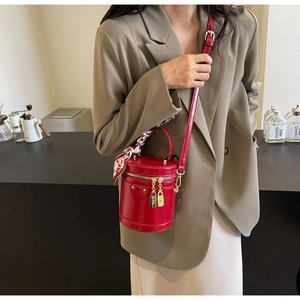 Détail du sac seau cylindrique rouge brillant avec ferrures dorées et poignée en soie