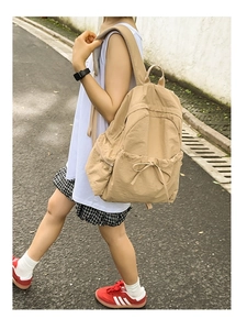 Side view of khaki nylon backpack with bow drawstring detail worn by a model in a street setting
