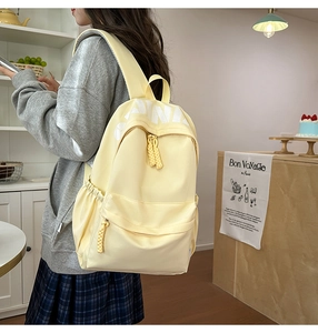 Detail of yellow nylon backpack featuring white letter prints and woven zipper pulls