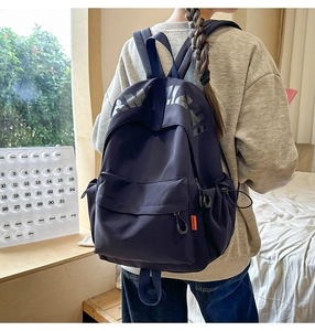 Detail of navy blue nylon backpack with large letter print and orange woven label