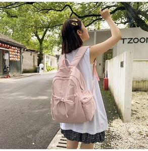 Detail of light pink student backpack with bowknot design and zip pocket on outdoor model