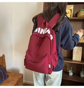 Detail of burgundy nylon backpack with JINA print shown in a lifestyle outdoor setting