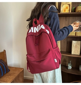 Close-up of burgundy canvas backpack featuring white CHINA letter print and woven rope zipper