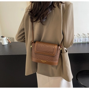 Détail d'un sac à bandoulière en cuir marron à texture tressée et lettrage doré