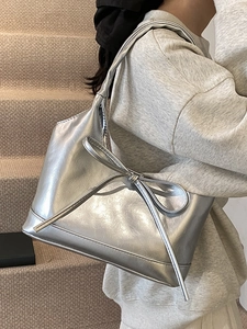 Silver metallic leather shoulder bag with bow detail worn by model on stairs