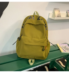 Detail of mustard yellow nylon backpack side pocket with orange label and woven zipper pull