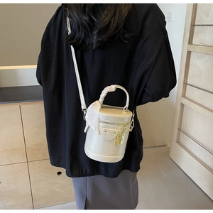 Détail du sac seau cylindrique crème avec poignée en foulard et dorures chic