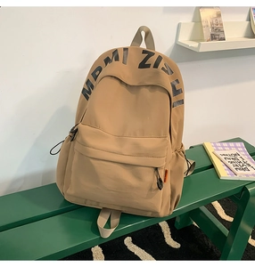 Detail of khaki nylon backpack with large black letter print on green wooden bench