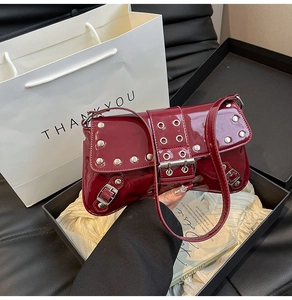 Detail of burgundy punk style underarm bag with silver rivets in a gift box