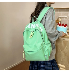 Detail view of mint green backpack featuring decorative white letters and side pocket