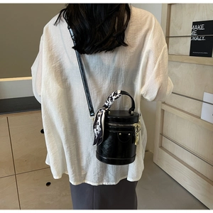 Détail du sac seau cylindrique noir brillant avec foulard floral décoratif et chaîne dorée