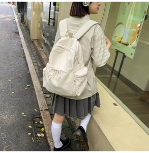 Outdoor shot of a minimalist cream nylon backpack with side pockets and bow details
