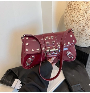 Detail view of burgundy patent leather underarm bag with silver punk rivets and buckles