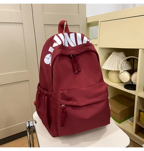 Close-up of burgundy school backpack with letter print and woven rope zipper pull