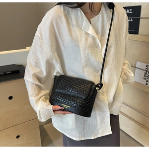 Détail du sac seau noir tressé avec boucle dorée et texte de mode élégant sur le rabat